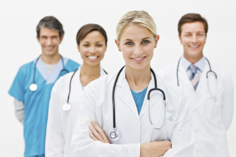 Beautiful young doctor standing with hands folded and assistant doctors in background